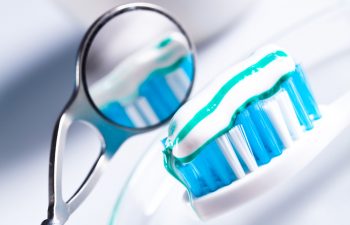 A dental mirror next to a toothbrush with toothpaste