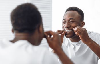 Afro-American man flossing his teeth in front of a bathroom mirror.